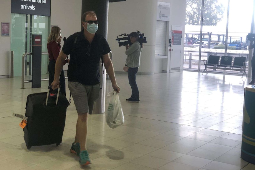 A passenger arrives at Perth Airport wearing a facemask and carrying his luggage.