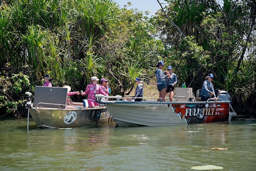 Eight women stand on two aluminium boats and hand each other drinks