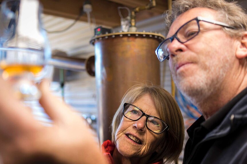 Matthew and Julie Cooper look at a glass of whisky they made, Tasmania 2019.