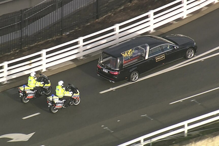 An aerial shot of a black hearse followed by two WA Police motorbikes.