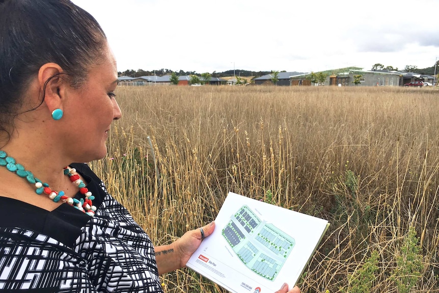A woman stands in front of an empty block holding a development map.