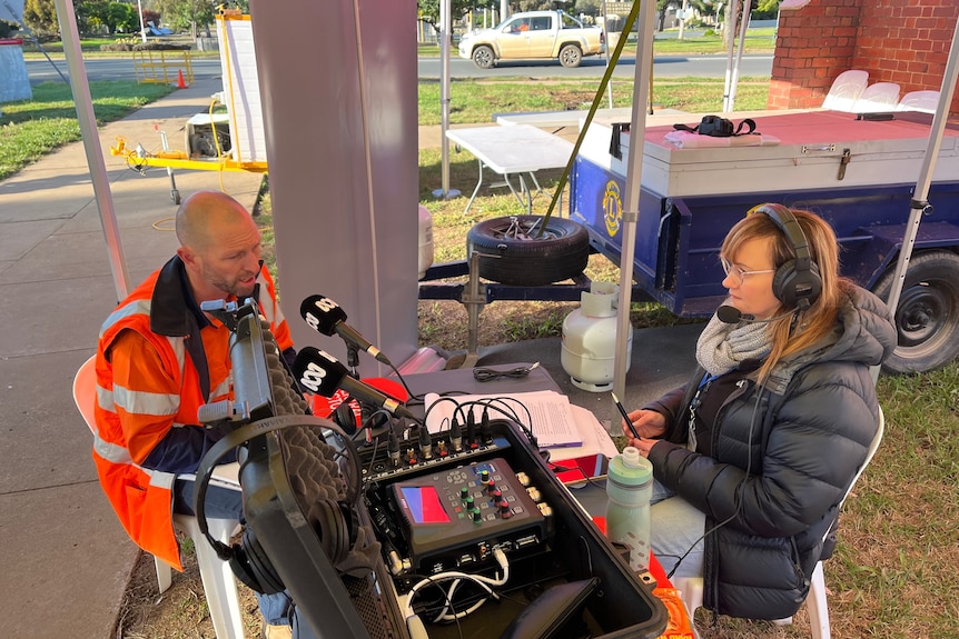 A man in high vis is interviewed by a woman with a microphone.