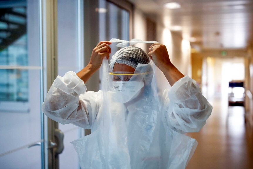 A female health worker puts on PPE in a hospital corridor.