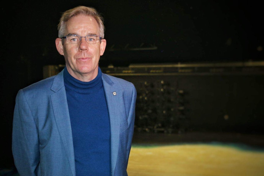 Mr Shirley stands on a stage with the background lit.