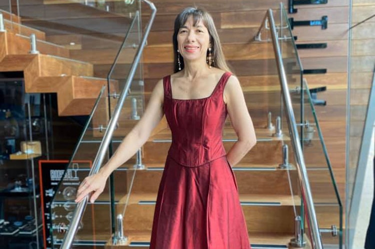 Darlene Chin dressed in a red formal dress, standing in a stairwell.