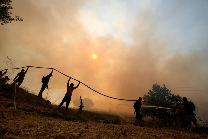 Firemen hold a hose amid a cloud of smoke