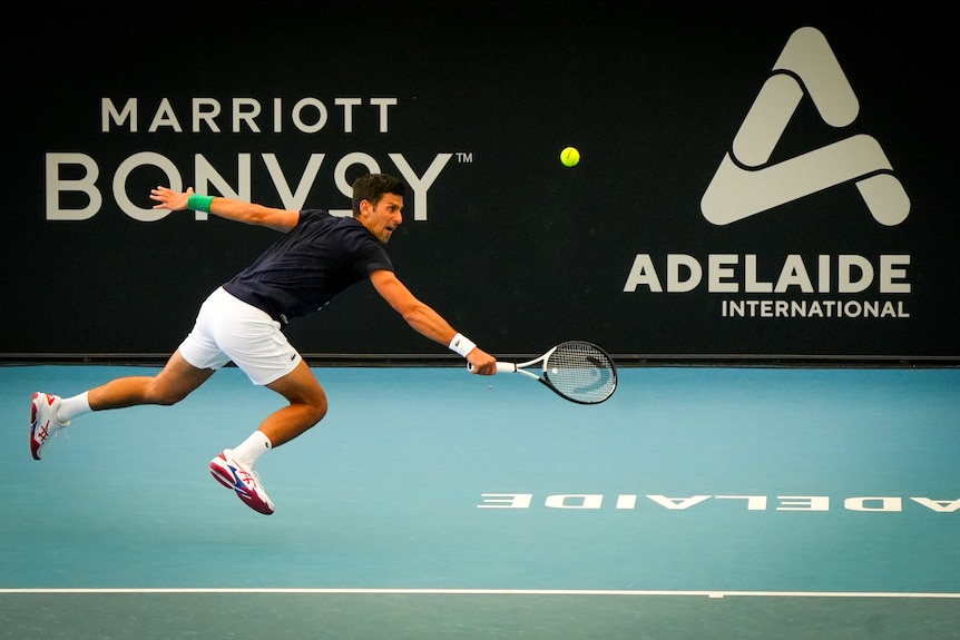 A man leaps to hit a ball with a tennis racquet in front of an Adelaide International banner