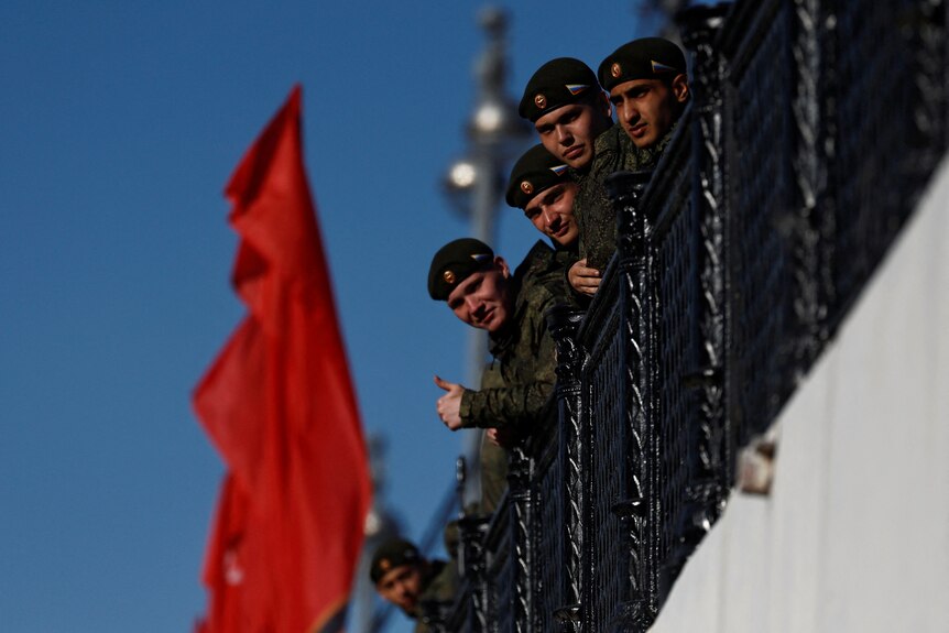 Soldiers leaning over a balcony with a red flag in the background