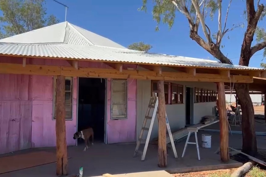 The front of an old building, half covered in pink sheets, the other tin.