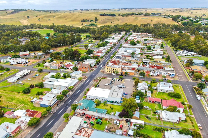 An aerial photo of lots of old buildings and houses lining a long street surrounded by big trees and rolling hills.