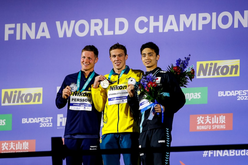 Three male swimmers pose with their medals after a race