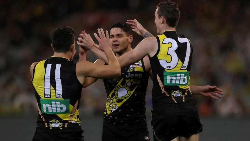 Dion Prestia and two Tigers teammates give each other high fives as they celebrate a goal against Essendon.