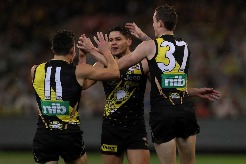 Dion Prestia and two Tigers teammates give each other high fives as they celebrate a goal against Essendon.