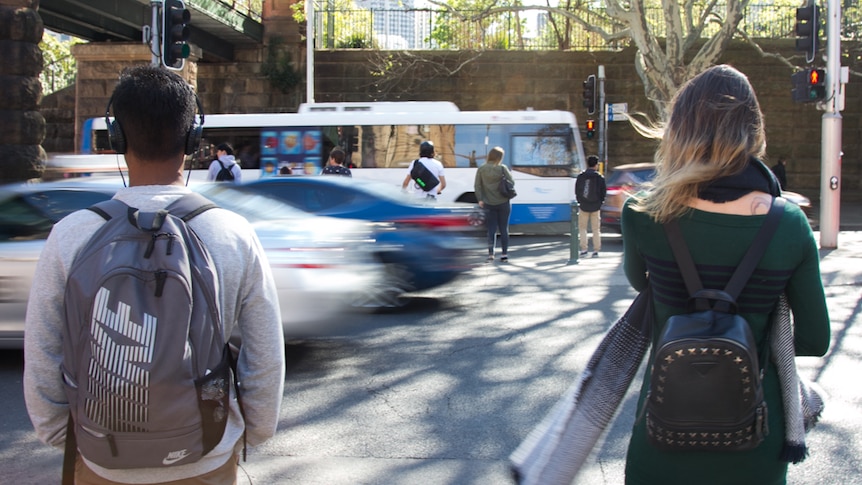 Two people stand waiting to cross at the pedestrian crossing