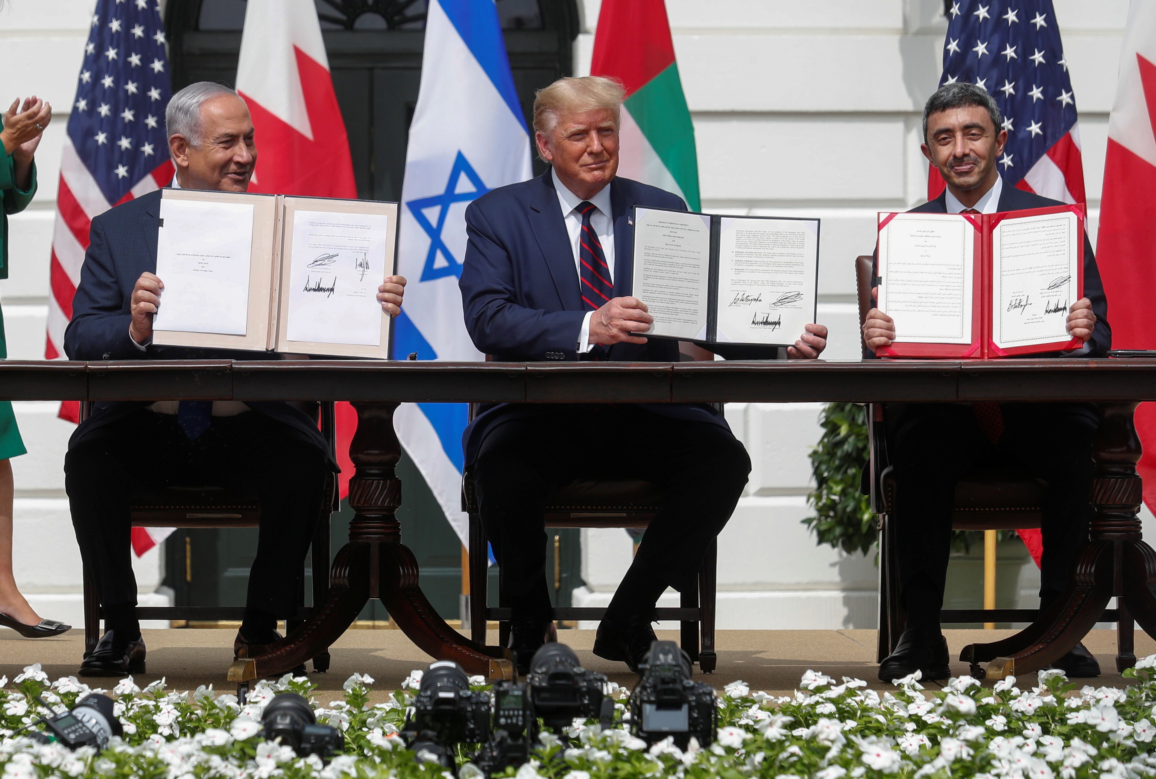 A photo of Benjamin Netanyahu, Donald Trump and Abdullah bin Zayed sitting at a long table, holding up copies of signed deals