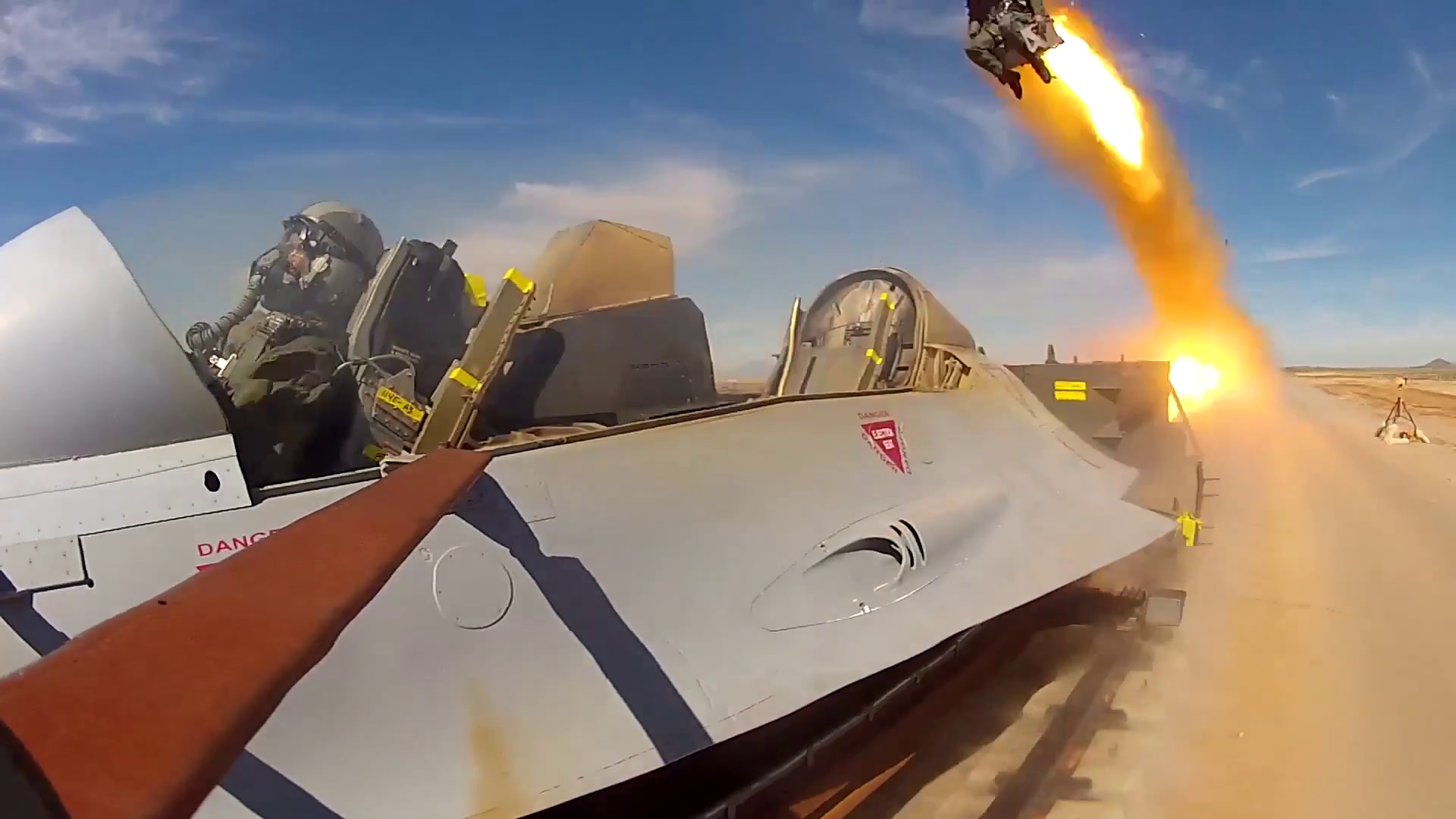 A vehicle resembling a cockpit on a track in the desert. A seat in the background appears to be blasting off in the background.