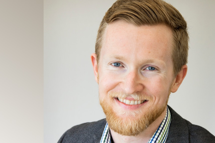 A man with a ginger-beard and a full head of neatly-groomed hair smiles at the camera.