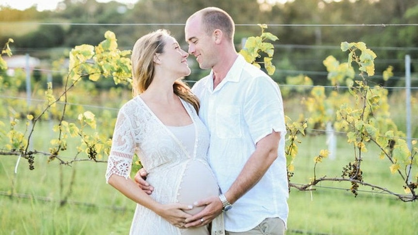 A man and a pregnant woman embrace in a vineyard.