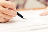 Elderly person signing a form with a fountain pen