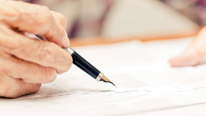 Elderly person signing a form with a fountain pen