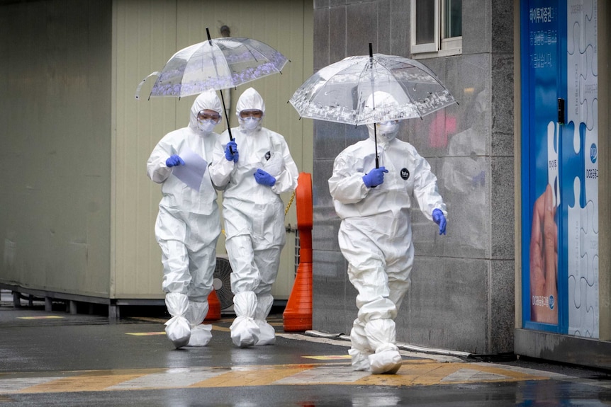 Three women in hazmat suits holding umbrellas