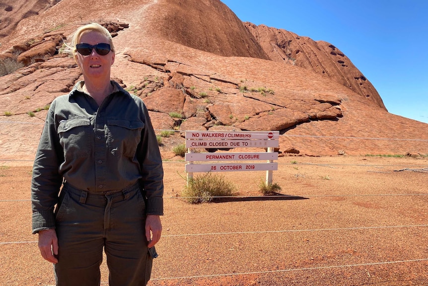 Lynda Wright is wearing a rangers uniform and standing in front of Uluru. There's a sign saying the climb is closed.