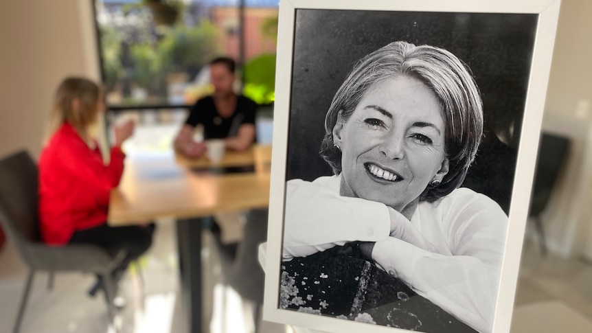 Picture frame with a black and white photo of an older woman in the foreground with a couple at a dinner table in the background