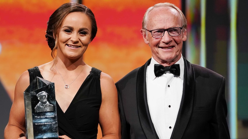 A smiling woman holds a trophy standing next to the son of the man the award is named after.