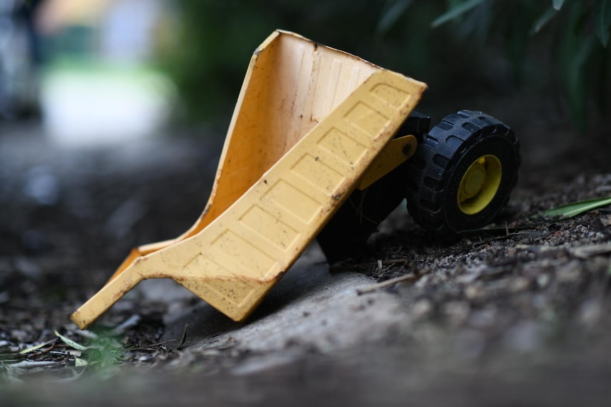 a broken yellow trailer from a toy truck with two wheels at the back sits in dirt