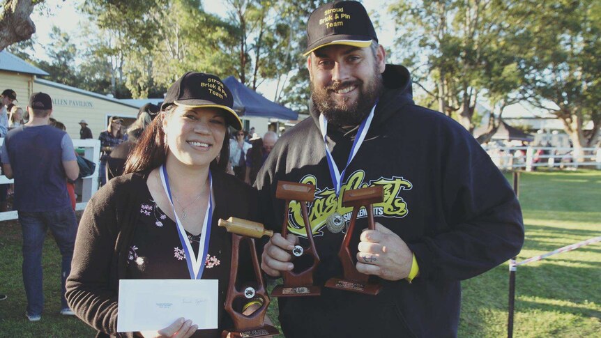 woman with a wooden trophy of a rolling pin and a man with wooden trophy of a brick