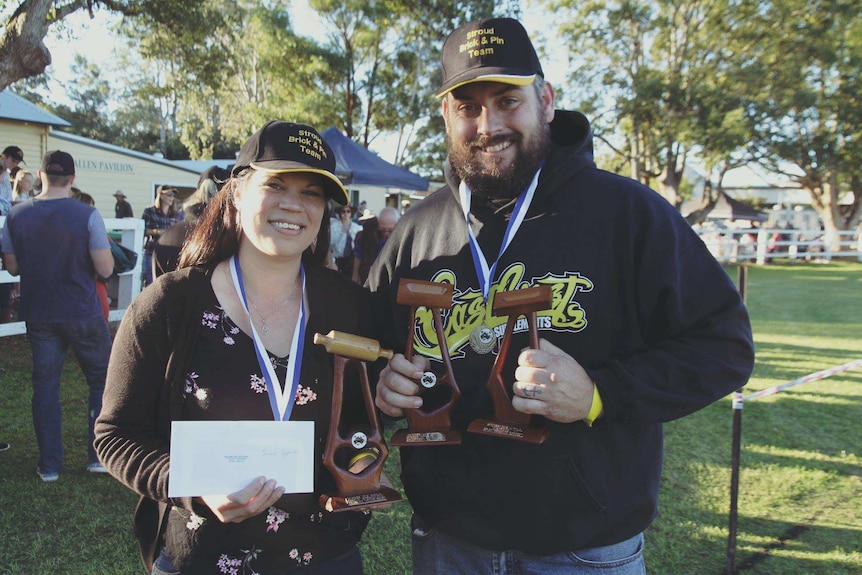 woman with a wooden trophy of a rolling pin and a man with wooden trophy of a brick