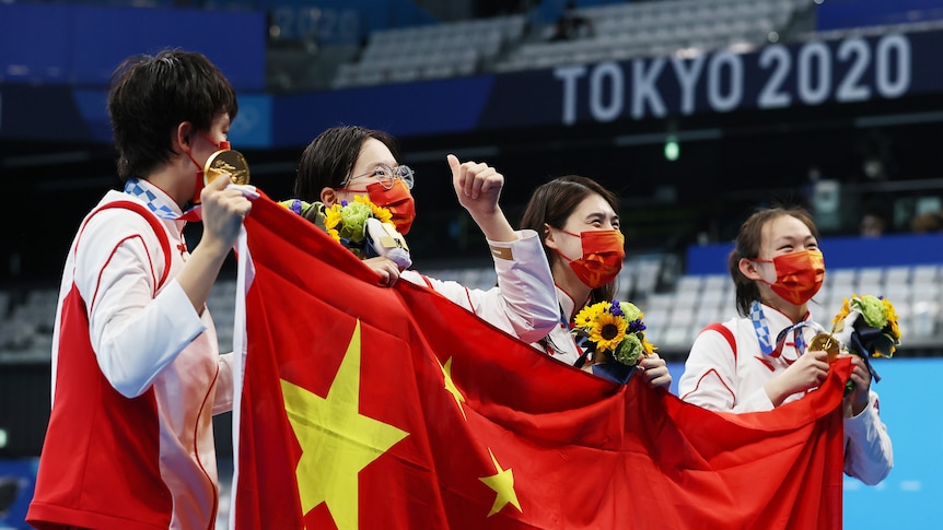 Four women wearing white hold up a red flag