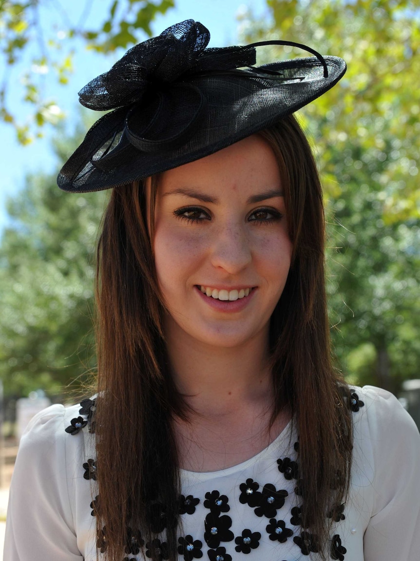 A portrait of Riharna Thomson dressed for race day in black hat and white dress.