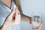 A woman holds a pill in one hand and a glass of water in the other.