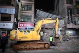 Rescuers work next to an excavator at a site where a building collapsed.