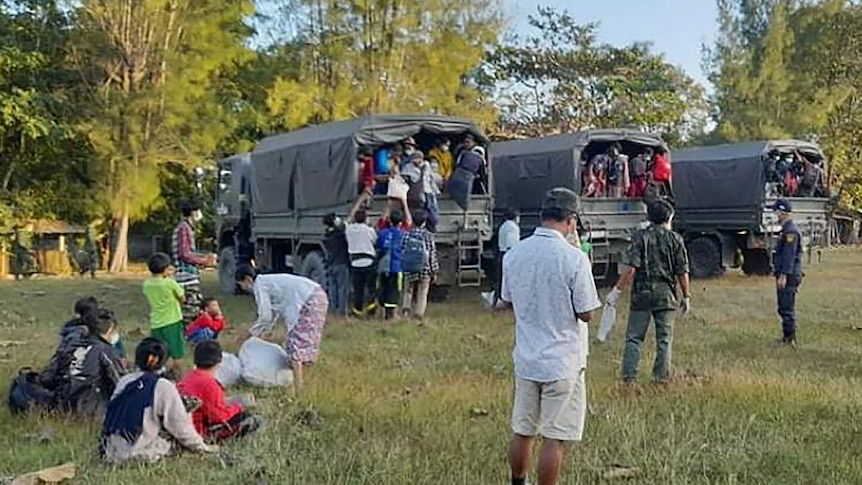 People stand and sit around on grass after getting out of army trucks. 