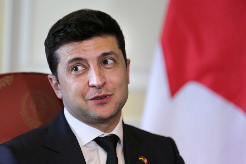 Volodymyr Zelenskiy looks to his right as he sits in a chair.