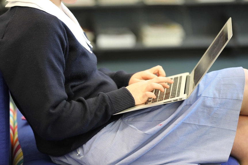 Una chica con uniforme escolar azul escribe en una computadora portátil.
