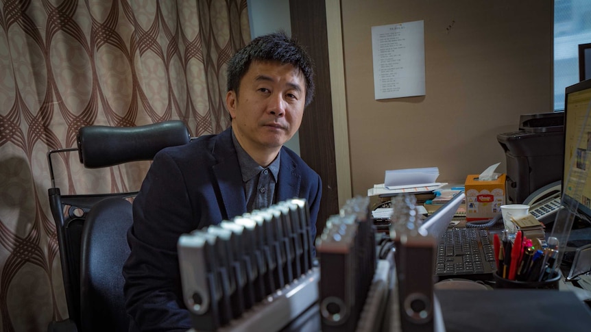 Chol Hwan Kang sits at a desk behind USB hubs used to clone USB sticks.