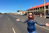 A woman with her arms outstretched with a pub in the background and a very wide road.