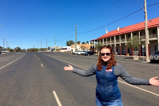 A woman with her arms outstretched with a pub in the background and a very wide road.
