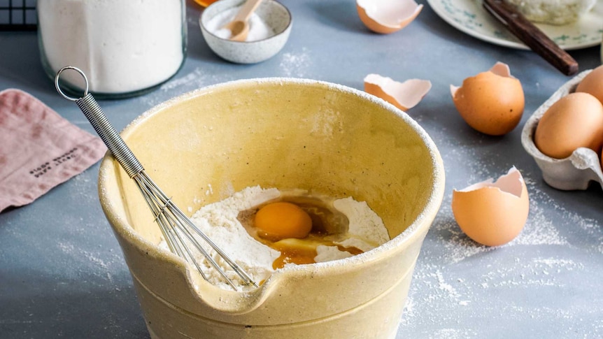 Eggs and flour in a large yellow mixing bowl on a table in an explainer on common baking terms like folding and blind baking.