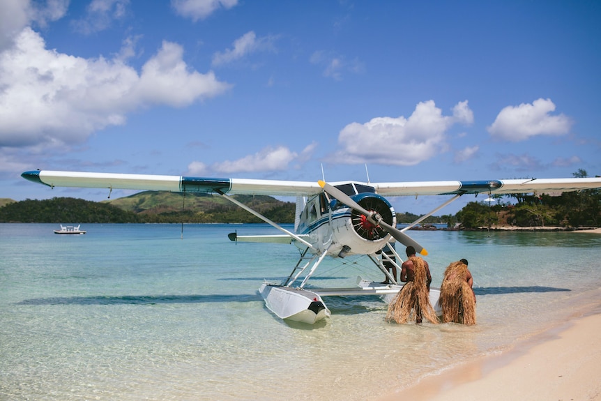 A seaplane on the shore of a tropical beach with two locals.
