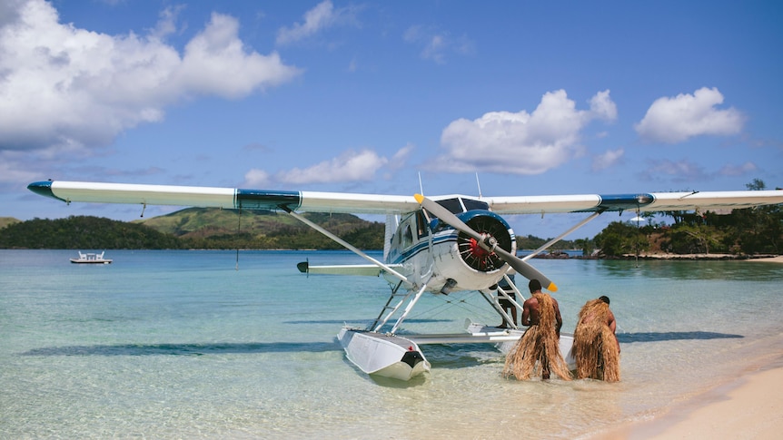 A seaplane on the shore of a tropical beach with two locals.