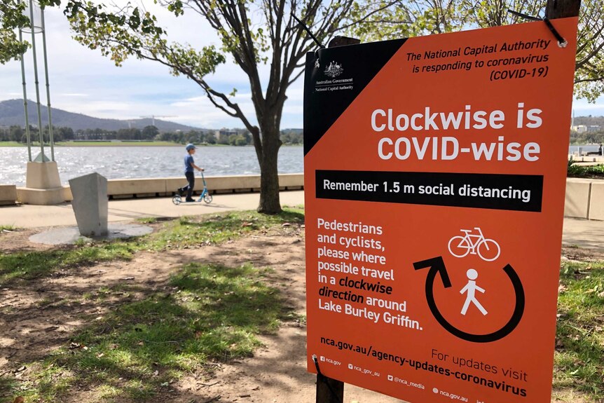 The sign says 'clockwise is COVID-wise' and the lake can be seen in the background.
