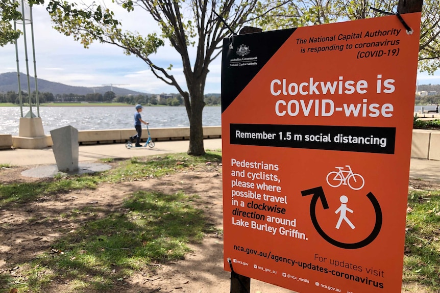 The sign says 'clockwise is COVID-wise' and the lake can be seen in the background.