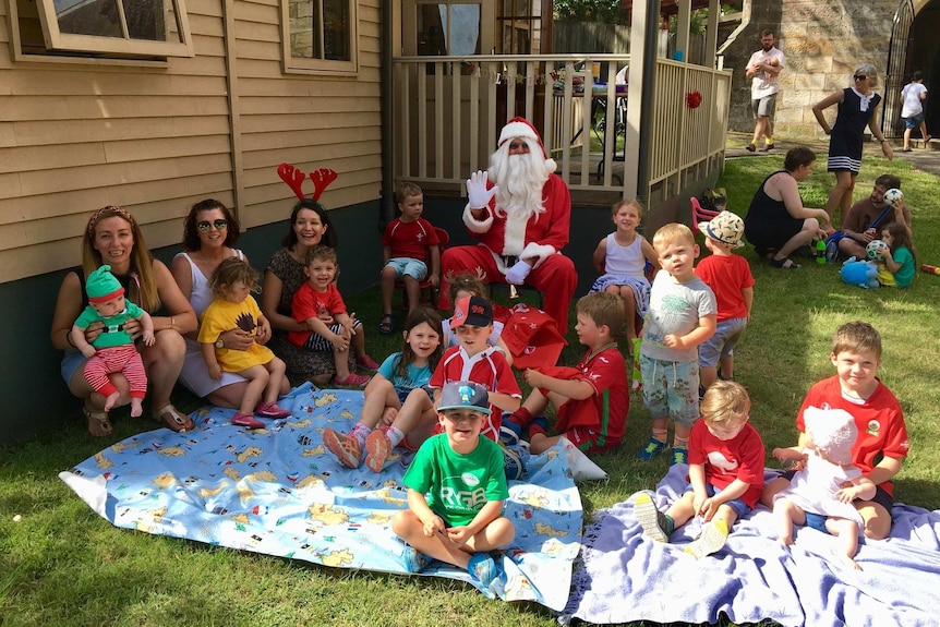 Santa with a group of laughing children outside on grass