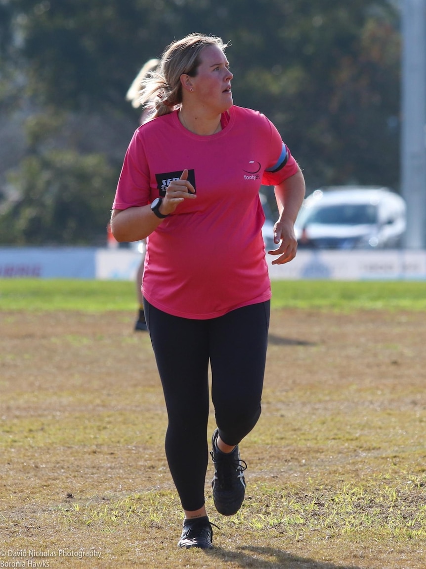 A woman in a pink top runs on an oval