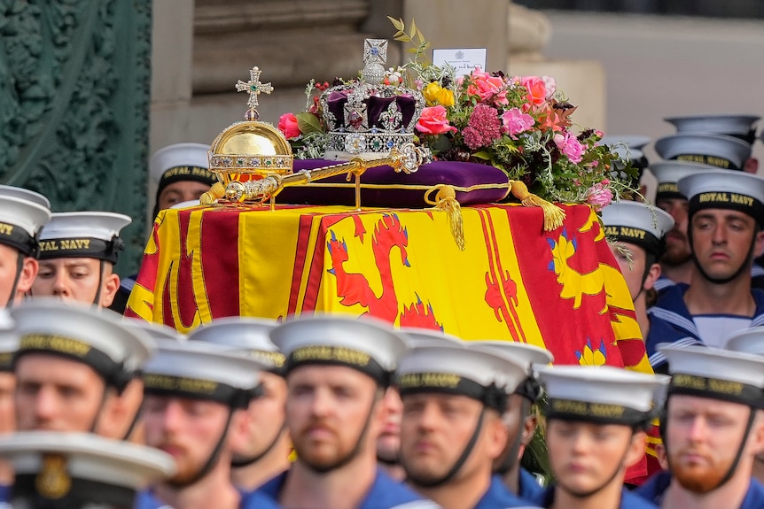 Navy members march through a street with the Queen's coffin. 