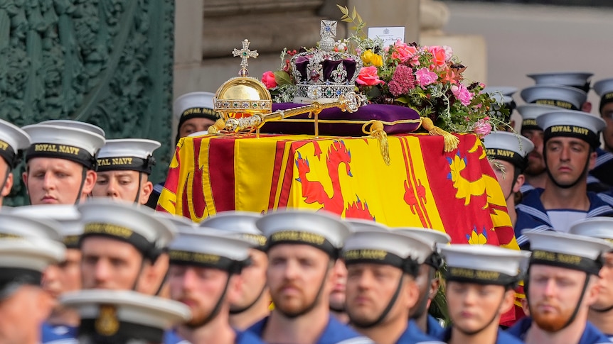 Navy members march through a street with the Queen's coffin. 